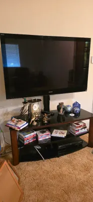 Sale Photo Thumbnail #19: Sony flat-screen television mounted above a black glass and wood entertainment stand filled with DVDs, books, and decorative accents.