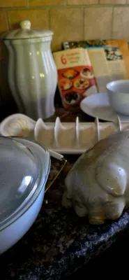 Sale Photo Thumbnail #38: Kitchenware arrangement including a ceramic pig figure, a glass-lidded casserole dish, a white taco holder, and a fluted canister.