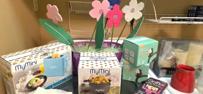 Sale Photo Thumbnail #32: Collection of small household items and novelty gifts including boxed MyMini appliances, stroller accessories, a selfie stick, LED candles, and decorative felt flowers in a bucket.