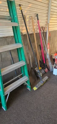 Sale Photo Thumbnail #52: Collection of outdoor lawn and garden tools, including a green fiberglass stepladder, various shovels, brooms, and a garden cultivator.
