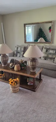 Sale Photo Thumbnail #6: Living room set featuring a beige upholstered sofa with pattern accent pillows, a dark wood coffee table, pair of woven urn-style table lamps, and a large ornate gold-framed wall mirror.