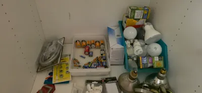 Sale Photo Thumbnail #25: Assorted household supplies inside a white shelf cabinet, including various batteries, light bulbs in a plastic bin, hardware items, and an appliance hose.