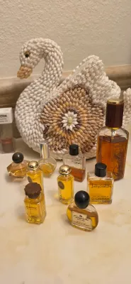 Sale Photo Thumbnail #66: Collection of vintage perfume bottles, including Hermès Equipage and D'Orsay Intoxication, arranged in front of a decorative seashell swan basket.