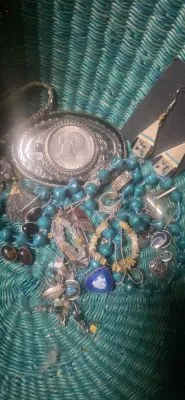 Sale Photo Thumbnail #14: Collection of assorted jewelry including a Bicentennial dollar belt buckle, stone pendants, beaded necklaces, and drop earrings in a green woven basket.