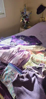 Sale Photo Thumbnail #50: Collection of women's purple clothing and accessories laid out on a bed, including a zip-up jacket, knit sweaters, and a floral sarong.