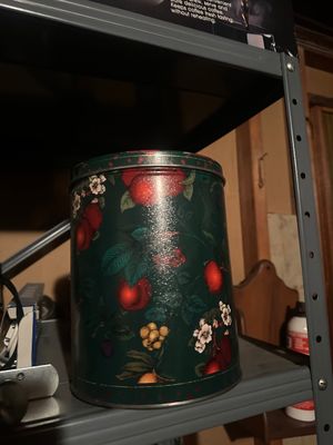 Sale Photo Thumbnail #40: Vintage dark green metal canister featuring a botanical fruit and floral pattern, stored on a metal utility shelf.