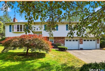 Sale Photo Thumbnail #106: Exterior view of a split-level home featuring white siding, brick lower accents, blue shutters, a two-car garage, and a Japanese maple in the front lawn.