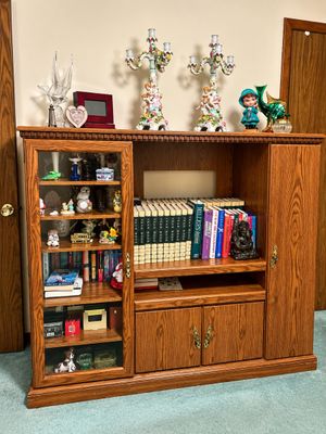 Sale Photo Thumbnail #9: Large wooden entertainment cabinet filled with books, knick-knacks, and decorative collectibles, topped with ceramic candelabras and figurines.