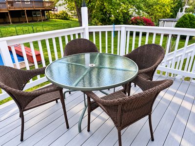 Sale Photo Thumbnail #19: Outdoor patio dining set featuring a round glass-top metal table surrounded by four brown resin wicker armchairs.