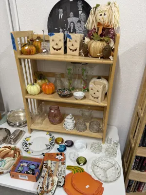 Sale Photo Thumbnail #13: A collection of Halloween decor, including jack-o'-lantern luminaries, a scarecrow doll, and Disney-themed kitchen accessories, alongside vintage glassware and silver-tone serving pieces.
