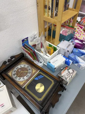 Sale Photo Thumbnail #27: Vintage wood wall clock with pendulum, alongside assorted household items including disposable face masks, light bulbs, and books.