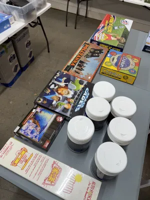 Sale Photo Thumbnail #12: Collection of board games and puzzles, including vintage Pollyanna, Cranium, and Space Cadets, displayed alongside multiple tubs of cleaning wipes and boxed auto sunscreens.