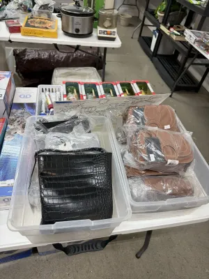 Sale Photo Thumbnail #8: Selection of new-in-plastic Rachel Zoe handbags in clear storage bins, including a black croc-embossed crossbody and cognac saddle bags.