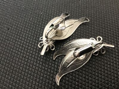 Sale Photo Thumbnail #188: Pair of vintage silver-tone clip-on earrings featuring a double leaf design with a flower motif accent. Includes textured vein detailing on the leaves. Measures approximately 1.5 inches in length. In good vintage condition with light wear consistent with 