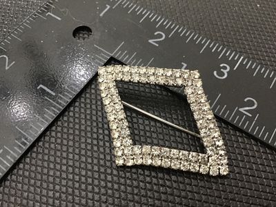 Sale Photo Thumbnail #102: A vintage diamond-shaped brooch featuring two rows of prong-set clear sparkling rhinestones set in silver-tone metal. Measures approximately 1.5 inches long by 1.25 inches wide. Features a standard pin back with rotating C-clasp mechanism. Good vintage co