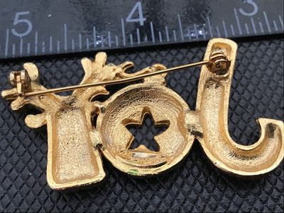 Sale Photo Thumbnail #12: A festive gold-tone Christmas brooch featuring the word 'JOY' spelled out with a candy cane for the 'J', a green enamel ornament with a star for the 'O', and a reindeer head for the 'Y'. Measures approximately 2 inches wide. Includes a rollover clasp on t