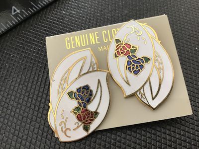 Sale Photo Thumbnail #160: Pair of vintage genuine cloisonné pierced post earrings featuring an elegant leaf shape with white enamel background, gold-tone accents, and colorful red, blue, and green rose floral motifs. Mounted on original display card marked 'GENUINE CLOISONNE'. In