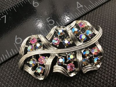 Sale Photo Thumbnail #108: A vintage mid-century silver-tone costume jewelry brooch featuring a stylized leaf or ribbon spray motif set with colorful aurora borealis rhinestones in pink, blue, and iridescent tones. Standard pin back mechanism with safety clasp. Measures approximate