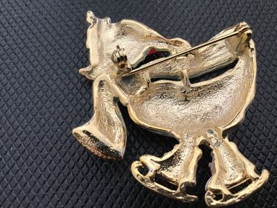Sale Photo Thumbnail #31: Vintage Christmas holiday brooch featuring an ice-skating white goose wearing a red Santa hat, green scarf, and ice skates with gold-tone accents. Crafted from enamelled metal with gold-tone backing and a standard pin back with safety clasp closure. Measu