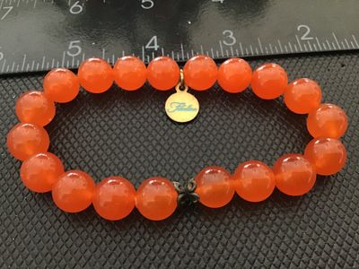 Sale Photo Thumbnail #44: A Fabulina stretch bracelet featuring vibrant translucent orange round beads with a round gold-tone logo charm tag and decorative end metal caps. Unstretched inner circumference measures approximately 6 to 6.5 inches. In good pre-owned condition with ligh