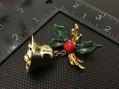 Sale Photo Thumbnail #96: Gold-tone Christmas holiday brooch pin featuring green enamel holly leaves, red berries, and a dangling gold-tone bell motif. Measures approximately 2 inches in size as shown with ruler. In good condition with minimal wear.