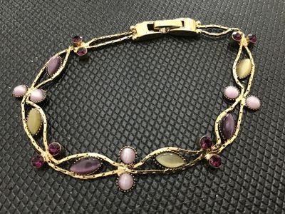 Sale Photo Thumbnail #122: Vintage gold-tone link bracelet featuring marquise and round cabochons in shades of purple, light pink, and yellow, accented with dark purple rhinestones. Features a fold-over clasp closure. Measures approximately 7 inches in length. In good vintage condi