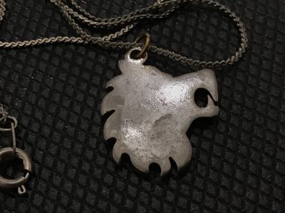 Sale Photo Thumbnail #116: A silver-tone necklace featuring a stylized lion head pendant filled with crushed turquoise chip inlay along the mane. The pendant hangs from a fine woven chain with a spring ring clasp. Shows light vintage wear and age-appropriate patina. Unmarked metal.