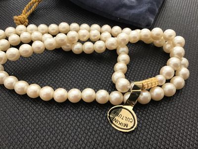 Sale Photo Thumbnail #178: Single-strand cream-colored faux pearl necklace featuring a gold-tone clasp and original gold tag marked 'MIKINI CULTURA' on one side and 'MADE IN JAPAN' on the reverse. Comes with a blue velvet drawstring pouch. Measures approximately 18-20 inches long w