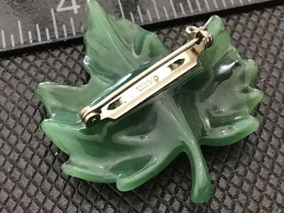Sale Photo Thumbnail #50: A vintage Avon costume jewelry brooch featuring a molded green resin leaf design (likely a maple leaf) set with a single small clear rhinestone dewdrop accent. The back pin hardware is marked AVON©. Measures approximately 1.5 inches. In good vintage cond