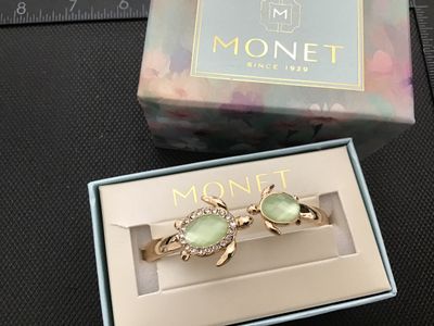 Sale Photo Thumbnail #52: A Monet gold-tone hinged cuff/bangle bracelet featuring two sea turtles with light green translucent cabochon shells and clear rhinestone accents around the larger turtle. Includes original Monet gift box. Features a spring hinge closure. Marked MONET on 