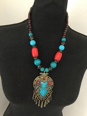Sale Photo Thumbnail #189: Boho style statement necklace featuring a large ornate brass-tone pendant with faux turquoise, coral-colored flower details, and dangling tassels. Strung with turquoise-blue and bright coral chunky beads alongside dark wood beads near the back. Features a