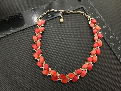 Sale Photo Thumbnail #99: Vintage gold-tone choker necklace featuring leaf-motif settings accented with alternating red and coral-tone navette/marquise lucite or glass cabochons. Includes an adjustable extension chain with a hook clasp and textured metal ball dangle. In good vinta