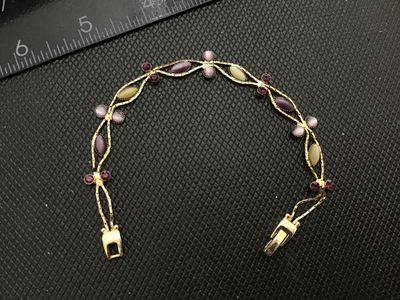 Sale Photo Thumbnail #121: Vintage gold-tone link bracelet featuring marquise and round cabochons in shades of purple, light pink, and yellow, accented with dark purple rhinestones. Features a fold-over clasp closure. Measures approximately 7 inches in length. In good vintage condi