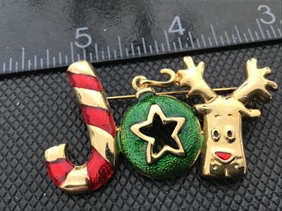 Sale Photo Thumbnail #11: A festive gold-tone Christmas brooch featuring the word 'JOY' spelled out with a candy cane for the 'J', a green enamel ornament with a star for the 'O', and a reindeer head for the 'Y'. Measures approximately 2 inches wide. Includes a rollover clasp on t