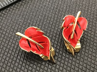 Sale Photo Thumbnail #165: Pair of vintage gold-tone clip-on earrings featuring vibrant red enamel leaf designs. Mid-century modern style motif. Shows minor wear to the enamel along some edges consistent with age and use. Gold-tone clip mechanisms appear intact and functional.