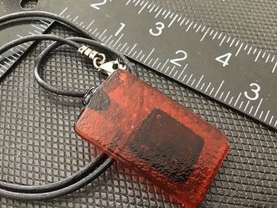 Sale Photo Thumbnail #112: Artisan dichroic fused glass pendant featuring layered iridescent purple, blue, and magenta tones. The rectangular pendant measures approximately 1.5 inches long and hangs from a black cord necklace with a metallic lobster claw clasp. In good pre-owned co