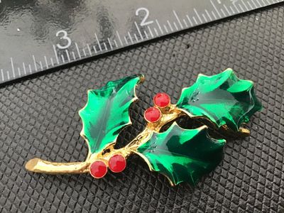 Sale Photo Thumbnail #18: A vintage gold-tone Christmas holly brooch featuring green enamel leaves and red enamel berries. Signed 'AJC ©' on the back. Includes a secure roll-over safety clasp. Measures approximately 2.5 inches long. In good vintage condition with minor wear consi