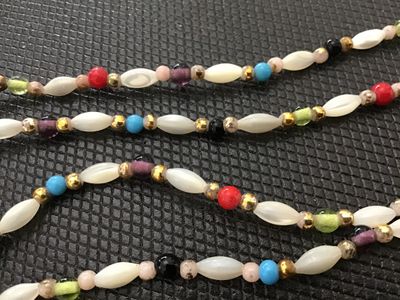 Sale Photo Thumbnail #97: Long beaded continuous necklace featuring white marquise/rice-shaped beads alternating with colorful accent beads in shades of turquoise blue, red, green, purple, black, and gold tone spacer beads. Measures approximately 30+ inches long in total strand le