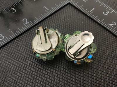 Sale Photo Thumbnail #83: Pair of vintage clip-on cluster earrings featuring light green crystal faceted beads with an aurora borealis iridescent coating. Measures approximately 1 inch in diameter each. Shows light signs of age and wear to metal backings consistent with vintage cl