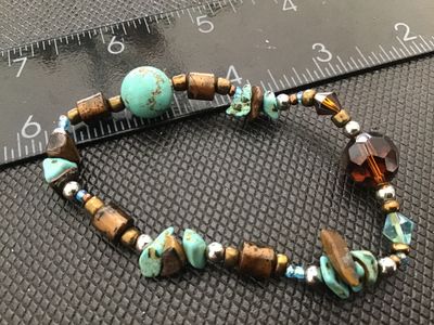 Sale Photo Thumbnail #55: A stretch beaded bracelet featuring faux or composite turquoise stones, tiger's eye-style chips, metallic spacers, and faceted iridescent glass or crystal beads. Measures approximately 7 inches in circumference. Good condition with light wear.