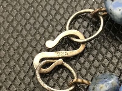 Sale Photo Thumbnail #57: A beaded necklace featuring blue stone nuggets/chunks interspersed with small dark accent beads. Features an S-hook clasp stamped '925' for sterling silver. Measures approximately 20-22 inches in total length. In good condition with natural inclusions and