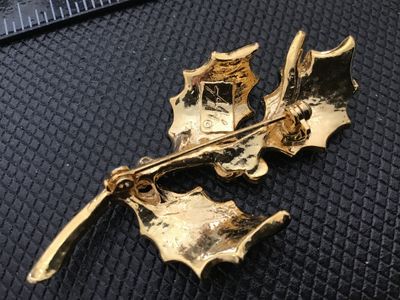 Sale Photo Thumbnail #19: A vintage gold-tone Christmas holly brooch featuring green enamel leaves and red enamel berries. Signed 'AJC ©' on the back. Includes a secure roll-over safety clasp. Measures approximately 2.5 inches long. In good vintage condition with minor wear consi