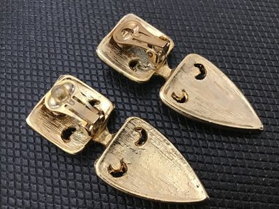 Sale Photo Thumbnail #128: A pair of vintage gold-tone clip-on earrings featuring a unique geometric and laced-toggle design. Each earring measures approximately 2 inches long. Good vintage condition with light wear consistent with age and use.