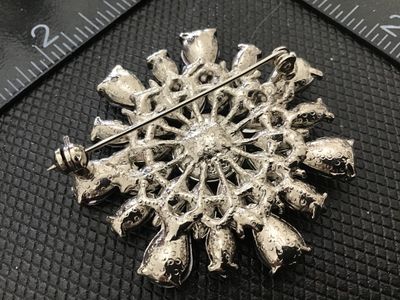 Sale Photo Thumbnail #170: Silver-tone costume brooch styled as a flower or starburst, featuring a dark purple central round rhinestone encircled by light purple and violet teardrop and marquise rhinestone accents. Secured with a standard pin stem and rollover clasp back. Measures 