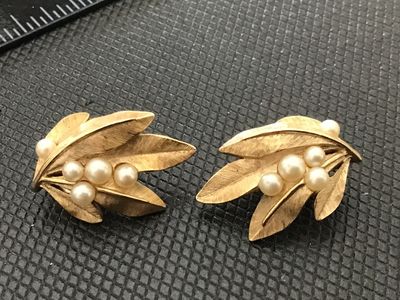 Sale Photo Thumbnail #181: A pair of vintage Crown Trifari clip-on earrings featuring a textured gold-tone leaf design adorned with faux pearl accents. Both earrings are stamped with the Crown Trifari copyright mark on the clip mechanisms. Show light surface wear consistent with ag