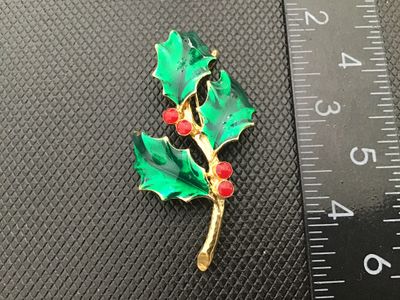 Sale Photo Thumbnail #20: A vintage gold-tone Christmas holly brooch featuring green enamel leaves and red enamel berries. Signed 'AJC ©' on the back. Includes a secure roll-over safety clasp. Measures approximately 2.5 inches long. In good vintage condition with minor wear consi