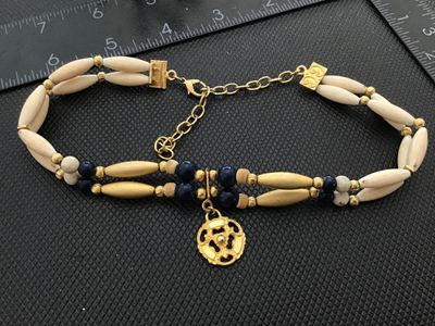 Sale Photo Thumbnail #73: Double strand beaded choker style necklace featuring off-white elongated rice/marquise beads, dark blue round accent beads, matte gold-tone center tubes, and ribbed spacer beads. Suspended at the center front is an ornate openwork filigree medallion penda