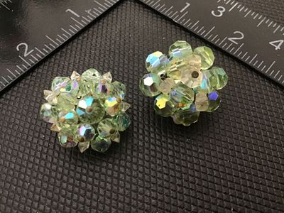 Sale Photo Thumbnail #82: Pair of vintage clip-on cluster earrings featuring light green crystal faceted beads with an aurora borealis iridescent coating. Measures approximately 1 inch in diameter each. Shows light signs of age and wear to metal backings consistent with vintage cl