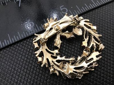 Sale Photo Thumbnail #61: Vintage gold-tone Christmas wreath pin featuring magenta metallic holly leaves, green pinecone accents, and red bead berries. Standard rollover safety clasp on the back. Measures approximately 1.75 inches in diameter. In good vintage condition with light 