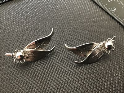 Sale Photo Thumbnail #187: Pair of vintage silver-tone clip-on earrings featuring a double leaf design with a flower motif accent. Includes textured vein detailing on the leaves. Measures approximately 1.5 inches in length. In good vintage condition with light wear consistent with 